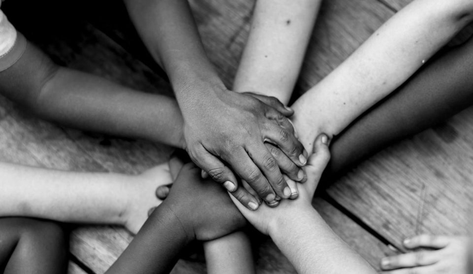 Viele Hände von Kindern und Erwachsenen liegen übereinander – ein Zeichen des Zusammenhalts